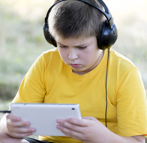 Boy in headphones looking tablet computer on the nature