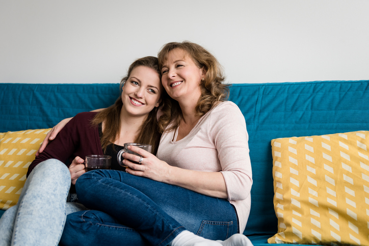 Mom witting with her daughter with ADHD on the couch, both of them are smiling and holding a cup of tea