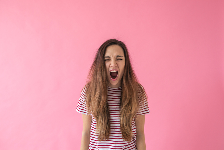 Defiant ADHD teen girl getting upset and yelling at the camera in front of a pink background