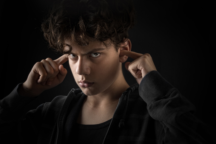 Teen with ADHD looking angry in a dark photo, with him plugging his ears with his fingers
