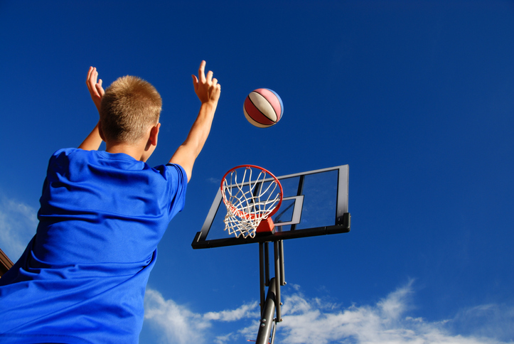 Neurodivergent teen taking a break from screens by shooting a basketball outside on the blue sky