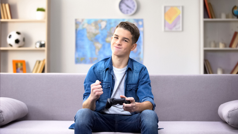 A teenage boy sit on a couch holding his controller and playing video games.