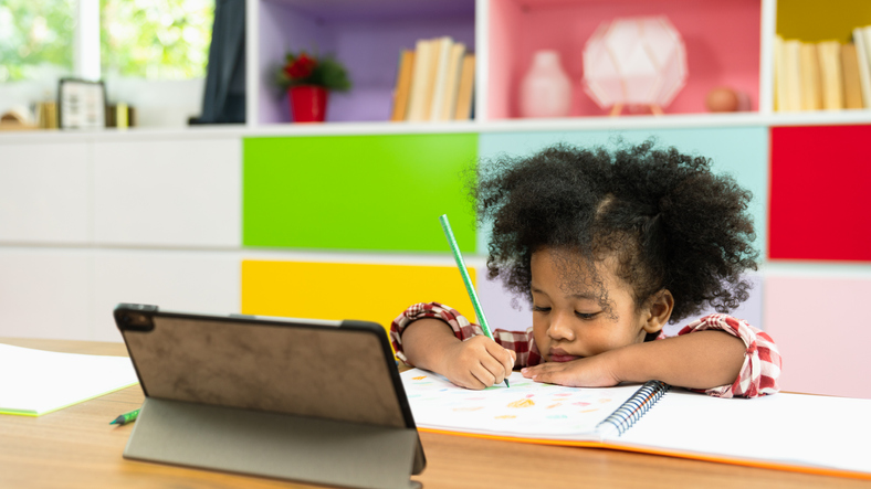 Young child drawing in a notebook at a table in front of a tablet showing the challenge of ADHD and screens