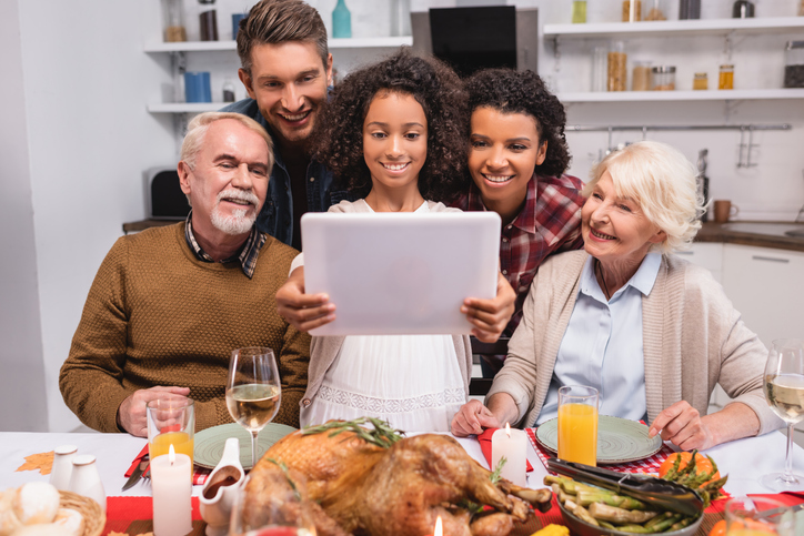 Family around the thanksgiving table, holding a tablet device to connect with other family member virtually.