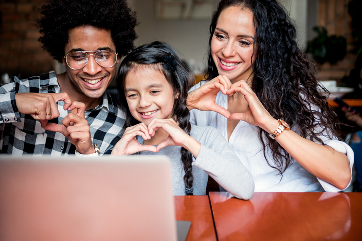 Family of three holding their hands in heart shapes as they have a zoom meeting with their family for new years