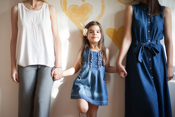 Child with ADHD standing between her divorced mothers and holding their hands with hearts drawn on the wall behind her