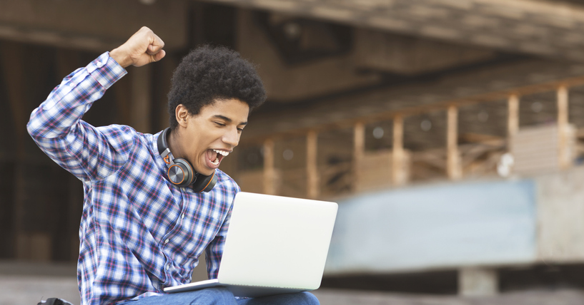 Teen with ADHD sitting outside on his computer holding his fist up with excitement about success and accomplishment