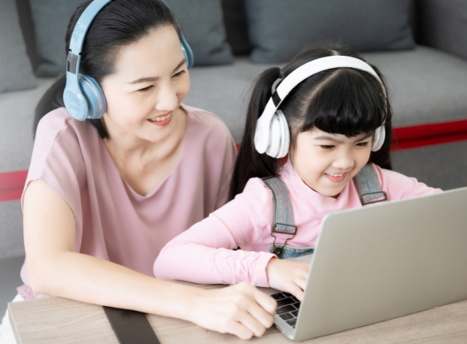 young girl doing work with mother on the computer with headphones on