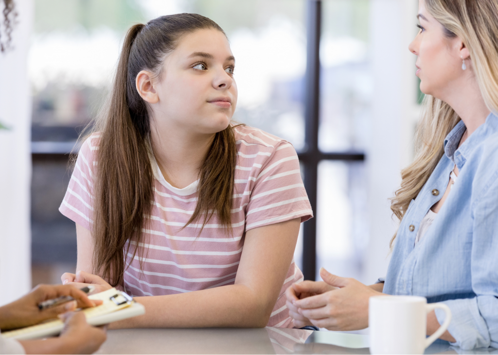 Teen girl with ADHD leaning over a desk and looking at her mother as they discuss returning back to school