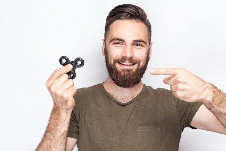 Adult male with ADHD holding up and pointing to his fidget spinner while smiling