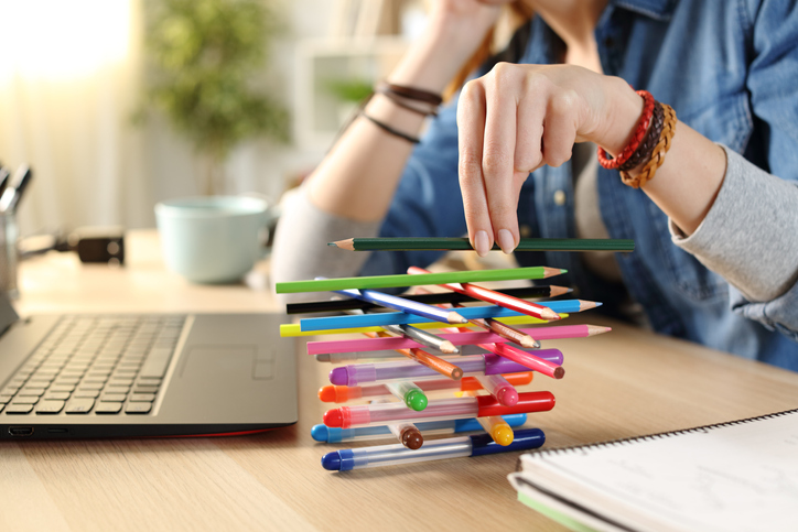 A person with ADHD working on building a pile of colorful pens next to a laptop at the table.