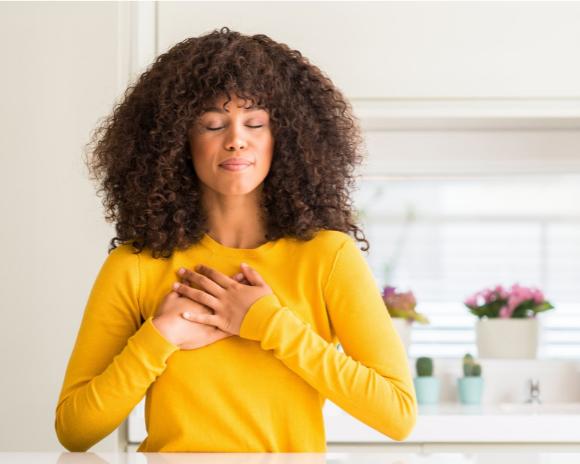 woman meditating in gratitude, holding her hands over her heart and smiling