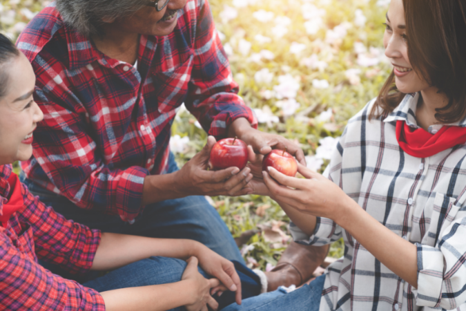 Family of three outside in flannel, smiling and sharing apples