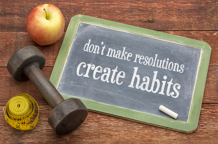 Small chalkboard that says "don't make resolutions, create habits," next to an apple and dumbbell weight.