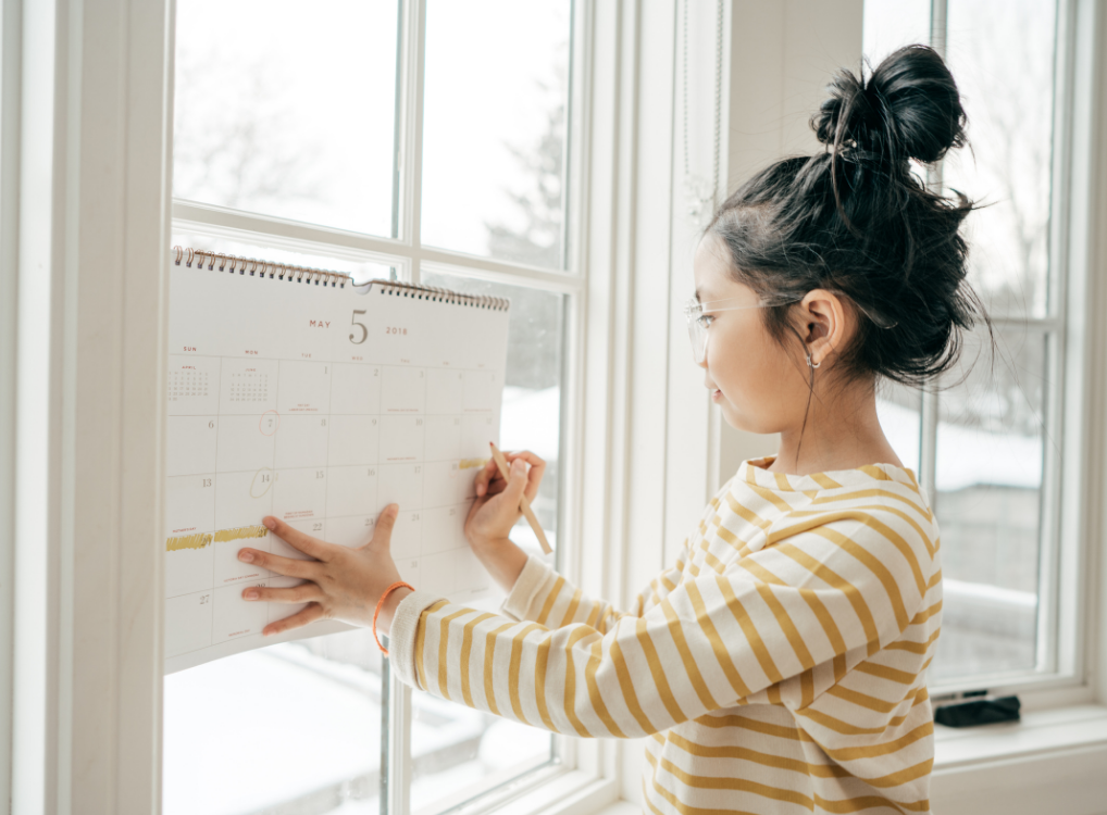 young girl writing on a family paper calendar