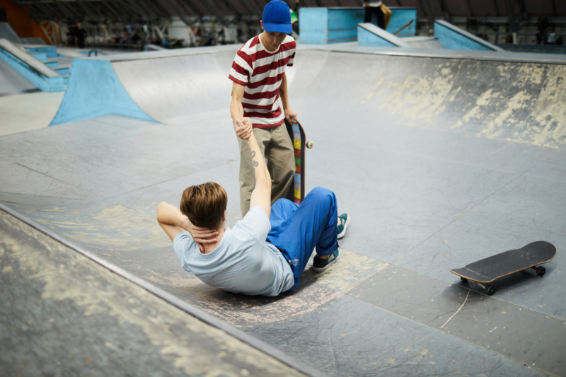 teen boy with skateboard helping friend get up