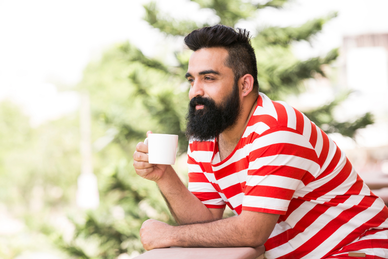 a man in a red and white striped shirt enjoying a cup of tea on the deck by a pine tree