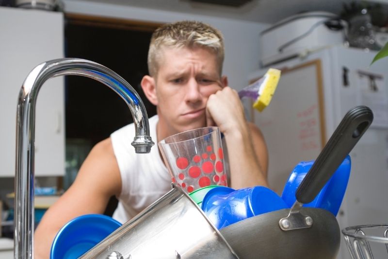 ADHD adult looking sad and unmotivated as he stares at a big pile of dishes in the sink.