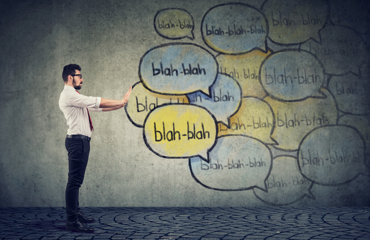 An adult professional standing in front of a wall with chalk drawing on it of speech bubbles that say "blah blah" in them.
