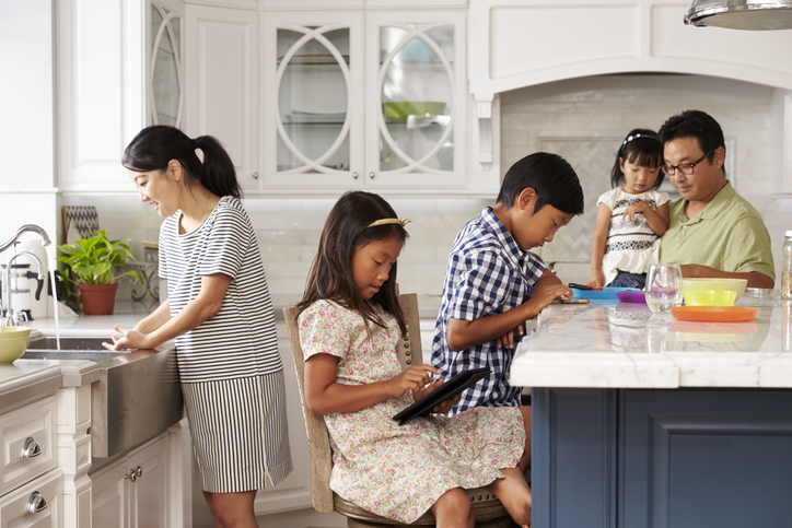 Family of two parents and three kids in the kitchen together, each focused on their own task or activity.