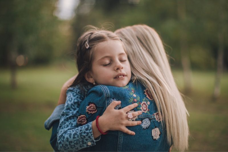 Parent/Woman hugging little girl near trees