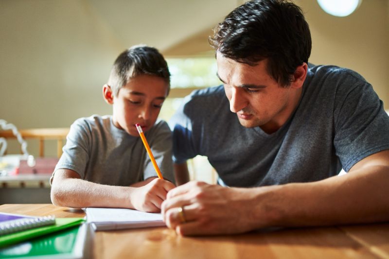 father watching son writing in notebook