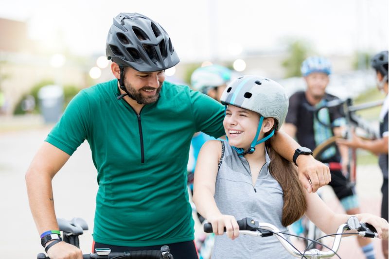 father with his arm around daughter in helmets at a bike race