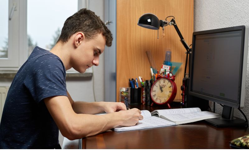 teen boy writing in notebook at clean and organized desk