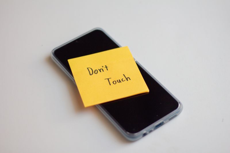 cell phone with yellow don't touch post-it on it