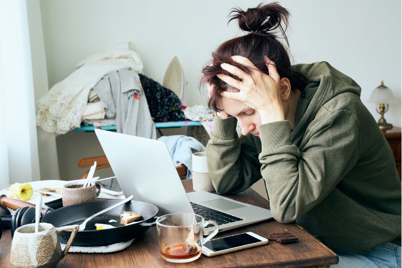 stressed woman in front of computer surrounded by laundry, dishes and food