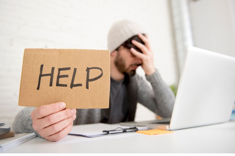 frustrated man in front of computer holding up help sign
