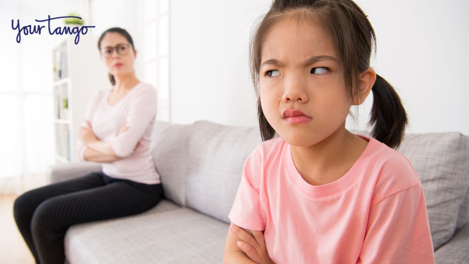 Little girl angry with her mother sitting on couch