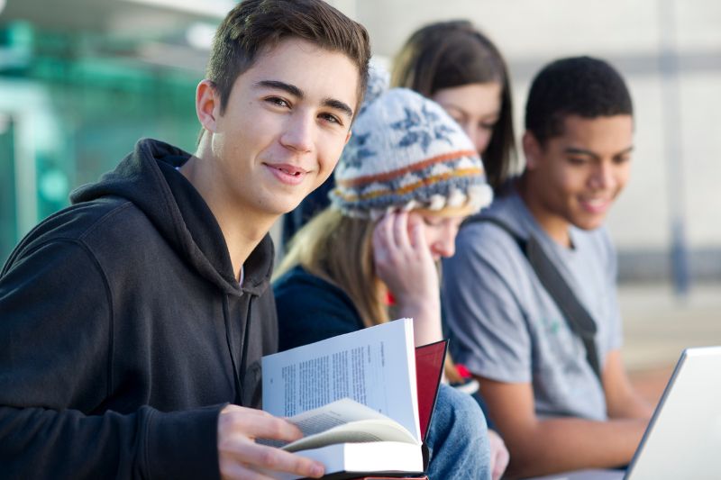 smiling teen boy with book and friends