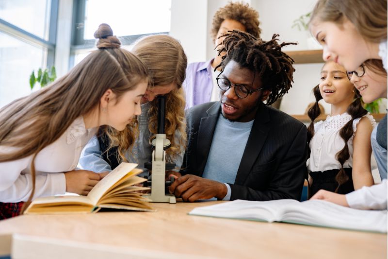 teacher with students looking at microscope