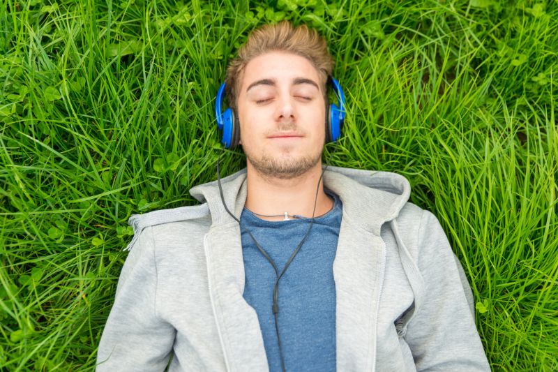 young man listening to music in grassy field